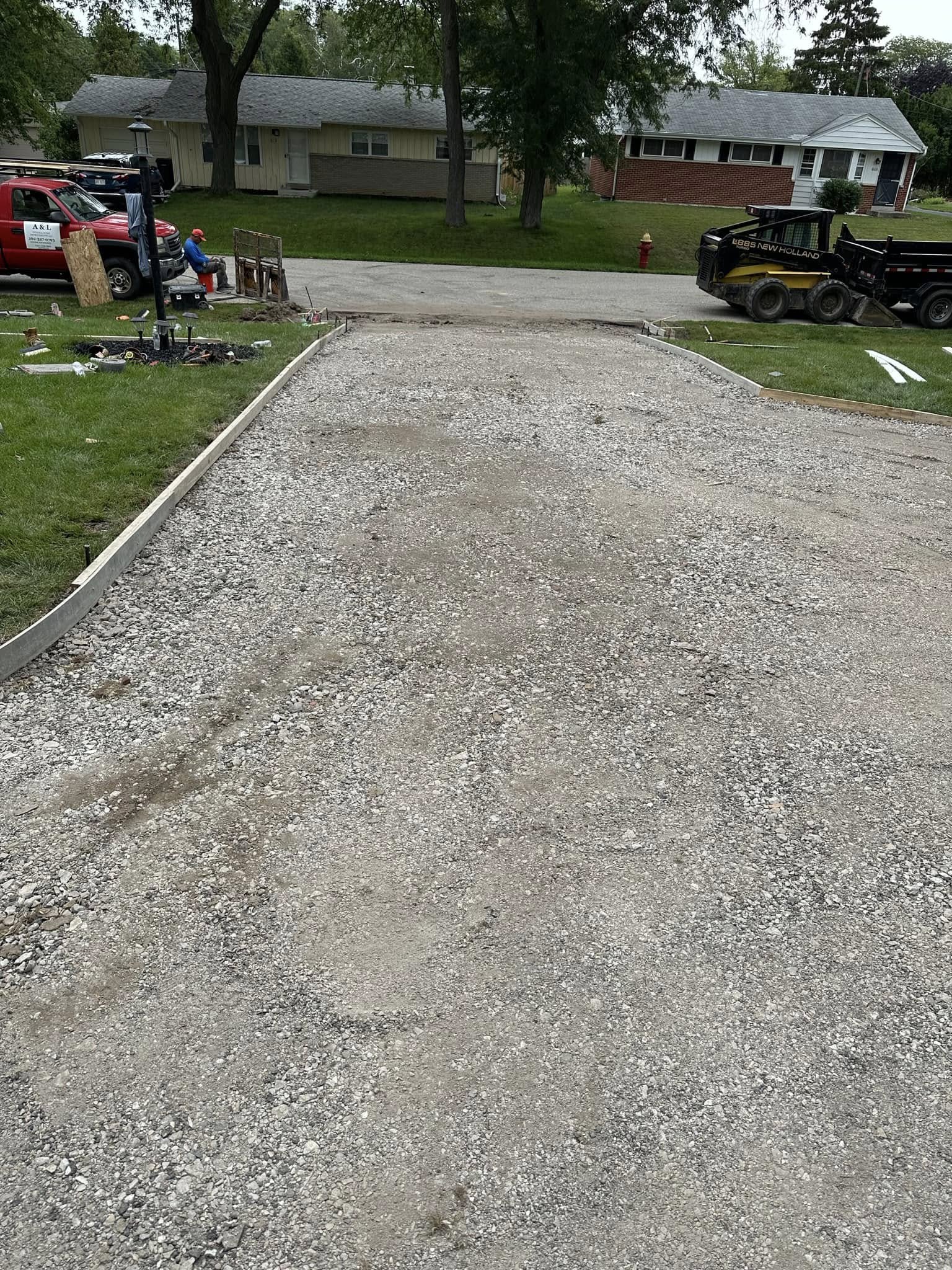 Gravel sub-base compacted and leveled for driveway with skid steer loader visible in background